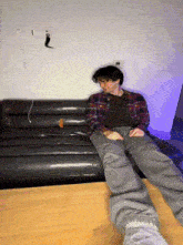 a man in a plaid shirt is sitting on a black couch