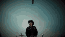 a man in a cowboy hat and sunglasses is standing in front of a plane flying in the sky .