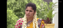 a woman in a yellow saree with a garland around her neck is sitting in front of a potted plant .