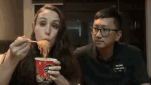 a man and a woman are eating noodles from a cup with chinese writing on it