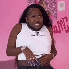a woman with a beard is wearing a white tank top and black shorts .