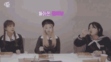 three girls are sitting at a table with boxes of food and a sign that says twice on it
