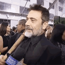 a man with a beard is holding a microphone while standing in a crowd of people .