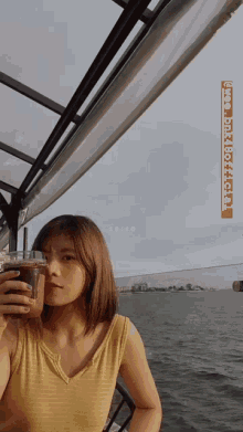a woman in a yellow tank top holds a cup of coffee in front of a body of water