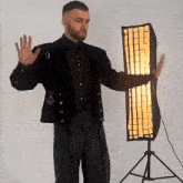 a man in a black jacket and black shirt is standing in front of a light .