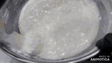 a close up of a white liquid in a metal bowl with the words made in animotica below it