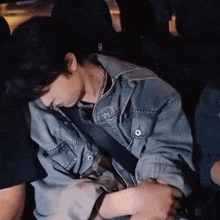 a man in a blue denim jacket is sleeping in the back seat of a car