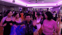a group of people are dancing in a room with purple lighting