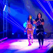 a couple of women are walking on a stage with a purple background .