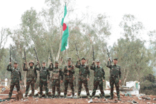 a group of soldiers holding guns in front of a green and red flag