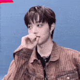 a young man wearing a brown striped jacket and a black shirt is covering his mouth with his hand .