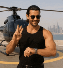 a man wearing sunglasses stands in front of a helicopter giving a peace sign