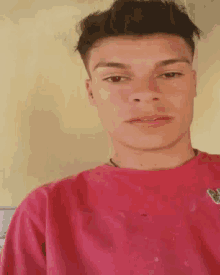 a young man is wearing a red shirt and looking at the camera .