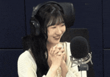 a woman wearing headphones and covering her face laughs in front of a microphone