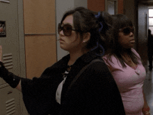 a woman wearing sunglasses is standing next to a woman wearing a pink shirt
