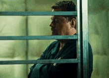 a man is standing behind bars in a prison cell looking out the window .