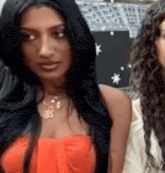 a woman with long black hair is wearing an orange top and necklace