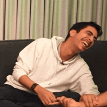 a man in a white sweatshirt is laughing while tickling another man 's foot