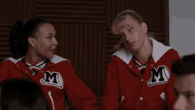 two cheerleaders wearing red jackets with m on them