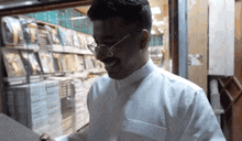 a man wearing glasses and a white shirt is standing in front of a glass door in a store .