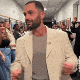 a man in a tan jacket is dancing in a hallway surrounded by people