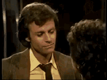 a man in a suit and yellow shirt is kissing a woman in a dark room .