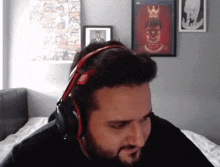 a man with a beard wearing headphones is sitting on a bed in a room .