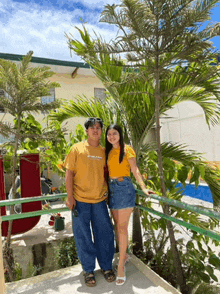 a man and a woman are standing next to each other on a balcony next to a palm tree .