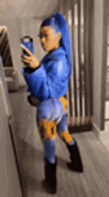 a woman in a blue jacket and pants is taking a selfie with her phone .