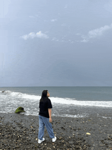 a woman is standing on a rocky beach looking out over the ocean
