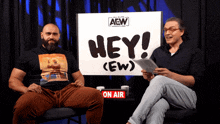 two men are sitting in front of a sign that says hey ( ew )