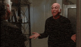 a bald man wearing glasses looks at himself in the mirror