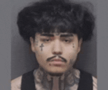 a man with a mustache and a cross tattoo on his face is looking at the camera .