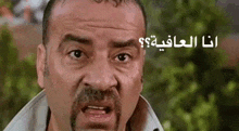 a man with a mustache is making a funny face with arabic writing on the bottom .