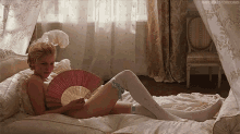 a woman laying on a bed holding a fan with the word bedrooms visible in the corner