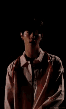 a young man wearing a pink shirt and red suspenders is standing in the dark .