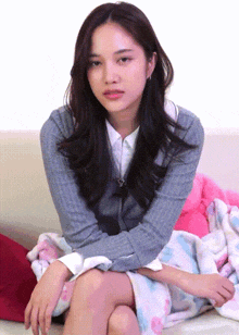 a woman in a grey sweater is sitting on a couch with her legs crossed