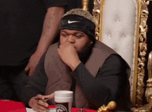 a man wearing a nike headband is sitting in a chair with a cup of coffee in front of him .
