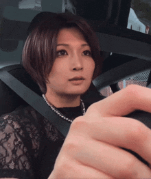 a woman wearing a black lace top and pearls is sitting in a car