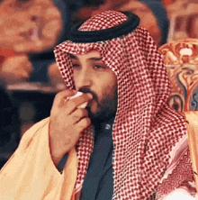 a man in a keffiyeh is smoking a cigarette while sitting on a chair .