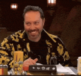 a man in a yellow and black jacket is smiling while sitting at a table with food .