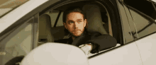 a man in a suit is sitting in the driver 's seat of a white car .