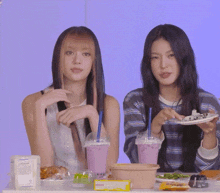 two girls are sitting at a table eating food and drinking