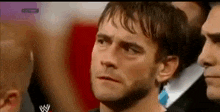 a close up of a man 's face with a wrestling logo on the bottom right corner .