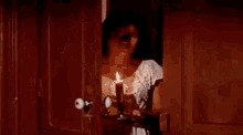 a woman in a white dress is holding a candle in her hand while standing in a doorway .