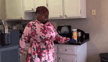 a woman in a floral robe stands in a kitchen