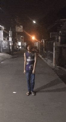 a person wearing a fly emirates shirt is dancing on a street at night