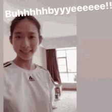 a woman wearing a white adidas shirt is smiling in front of a window