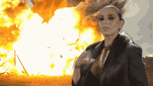 a woman stands in front of a large explosion with a sign in the background that says ' i 'm sorry '