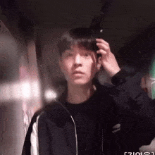 a man in a black jacket adjusts his hair in front of a mirror